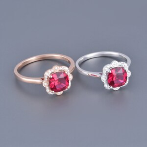 May include: Two rings featuring a red gemstone set in a halo of smaller white gemstones. One ring is rose gold and the other is silver.
