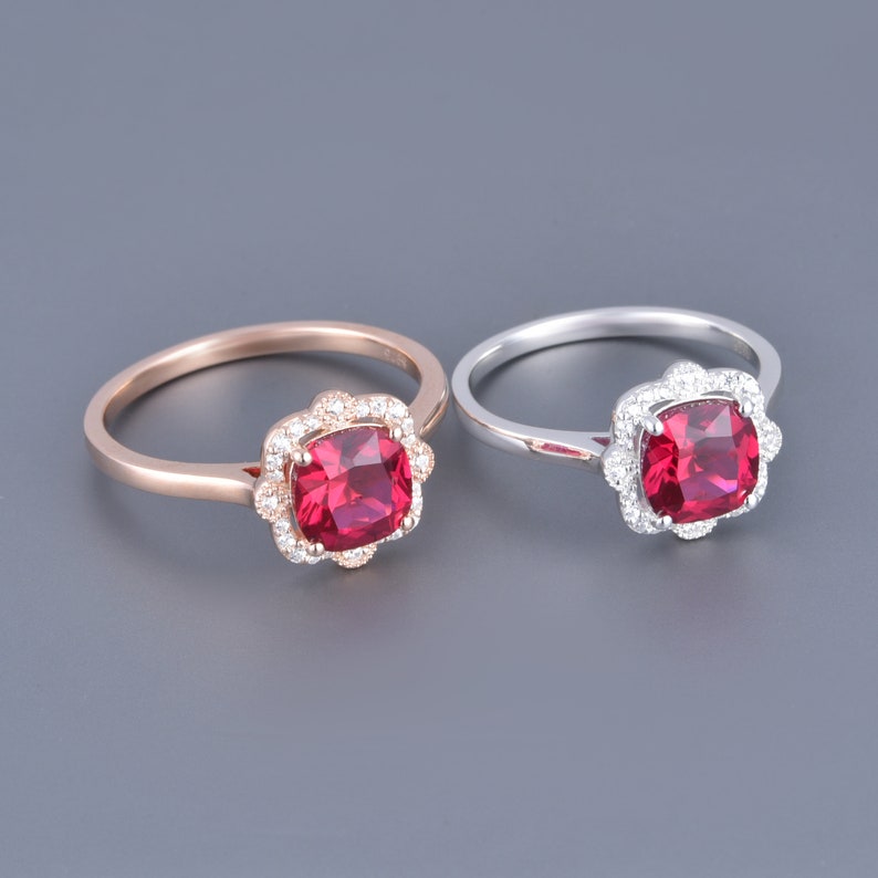 May include: Two rings featuring a red gemstone set in a halo of smaller white gemstones. One ring is rose gold and the other is silver.