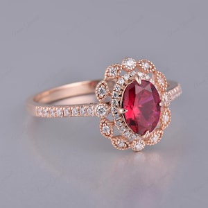 May include: A rose gold engagement ring with a large oval ruby surrounded by a halo of smaller diamonds. The band is also set with smaller diamonds.