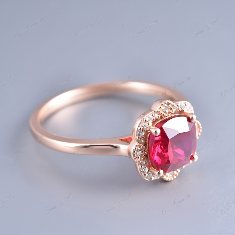 May include: A rose gold ring featuring a large, red, cushion-cut gemstone surrounded by a halo of smaller, white gemstones.