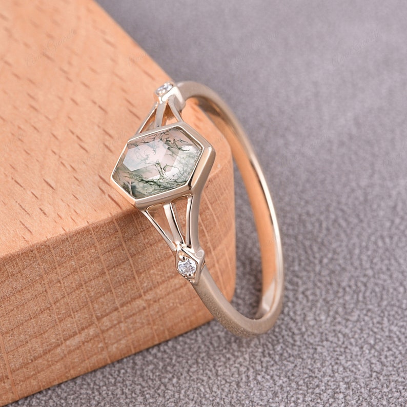 Puede incluir: Un anillo de oro con una piedra preciosa de &aacute;gata verde musgo engastada en un bisel hexagonal. El anillo tiene dos peque&ntilde;os diamantes a cada lado de la piedra principal.