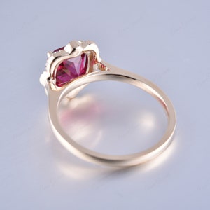 May include: A gold ring featuring a large, red, cushion-cut gemstone surrounded by smaller, white gemstones.