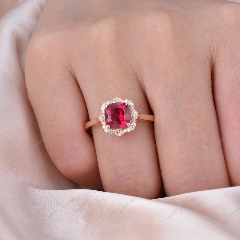 May include: A rose gold ring featuring a cushion-cut red gemstone encircled by a halo of smaller white gemstones.