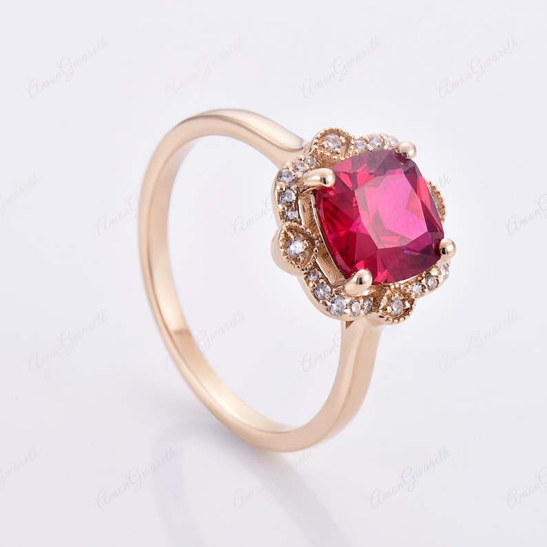 May include: A gold ring featuring a large, square-shaped red gemstone encircled by a halo of smaller, clear gemstones.