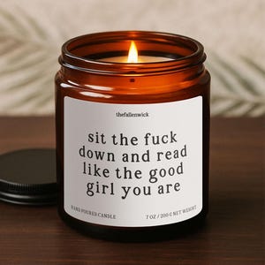May include: A lit candle in a brown glass jar with a black lid. The white label reads "sit the fuck down and read like the good girl you are." The candle is hand-poured and weighs 7 oz (200 g).