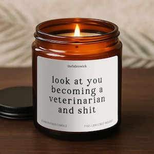 May include: An amber glass candle jar with a black lid and a lit wick. The white label reads "look at you becoming a veterinarian and shit." The candle weighs 200 g.