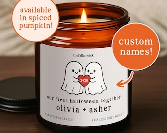 May include: A brown glass candle jar with a lit wick. The label features two ghost illustrations holding a heart with "2025" inside. Text on the label reads "our first halloween together olivia + asher" and "HAND POURED CANDLE". The candle is 7 oz / 200 g.