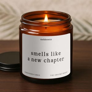 Peut inclure: Une bougie en verre ambré allumée avec un couvercle noir. L'étiquette blanche indique "smells like a new chapter". La bougie est coulée à la main et pèse 200 g.
