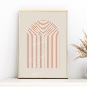 Op de afbeelding: Een ingelijste kunstdruk met een minimalistisch ontwerp van een terracotta boog op een beige achtergrond. Het kunstwerk wordt weergegeven op een wit oppervlak, met een vaas met gedroogde planten rechts.