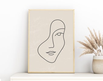 Könnte beinhalten: Gerahmter Kunstdruck mit minimalistischem Design. Er zeigt eine schwarze Strichzeichnung eines Gesichts auf beigem Hintergrund, eingefasst in einen goldenen Rahmen. Das Kunstwerk wird auf einer weißen Oberfläche präsentiert.