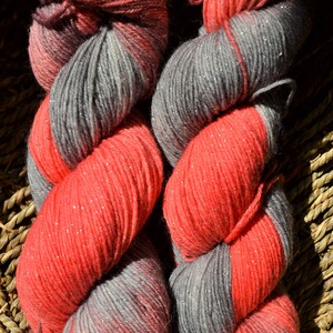 Puede incluir: Dos ovillos de hilo, uno rojo con purpurina plateada y otro gris con purpurina plateada. El hilo está enrollado en forma de bola y está listo para ser usado para tejer o hacer ganchillo.