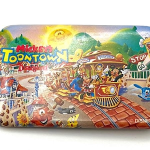 May include: Rectangular metal tray featuring a vibrant illustration of Mickey's Toontown at Disneyland. The artwork includes a train with Mickey, Minnie, and other characters, a sunny sky, and the text "Mickey's Toontown Disneyland".