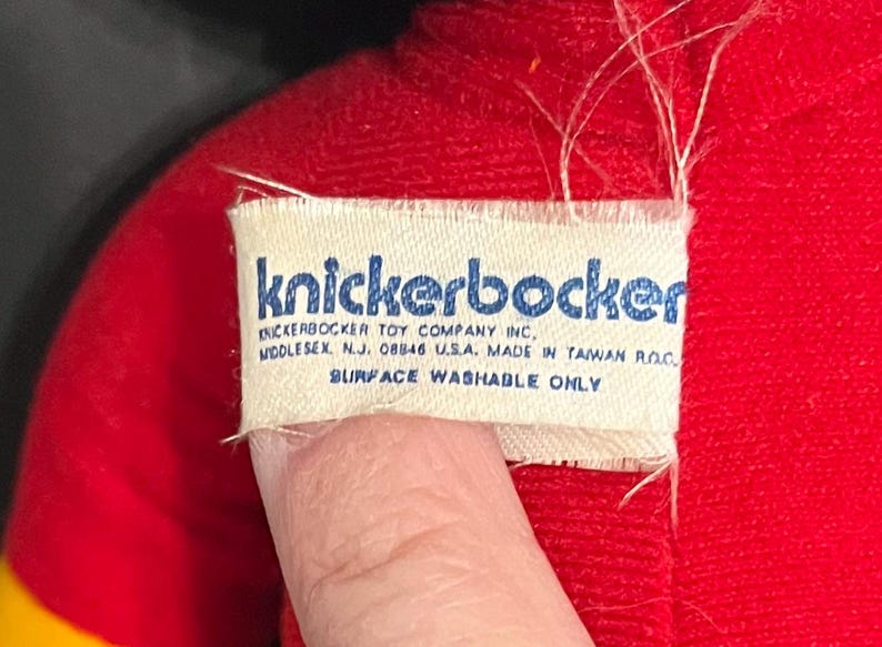 May include: A white tag with blue text that reads "knickerbocker" and "KNICKERBOCKER TOY COMPANY INC, MIDDLESEX. N.J. 08846 USA. MADE IN TAIWAN ROC SURFACE WASHABLE ONLY".