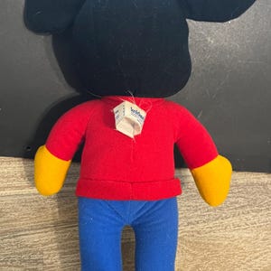 May include: A red and blue plush Mickey Mouse toy with a black head and yellow shoes. The toy has a tag that says "Kiddie" on it.