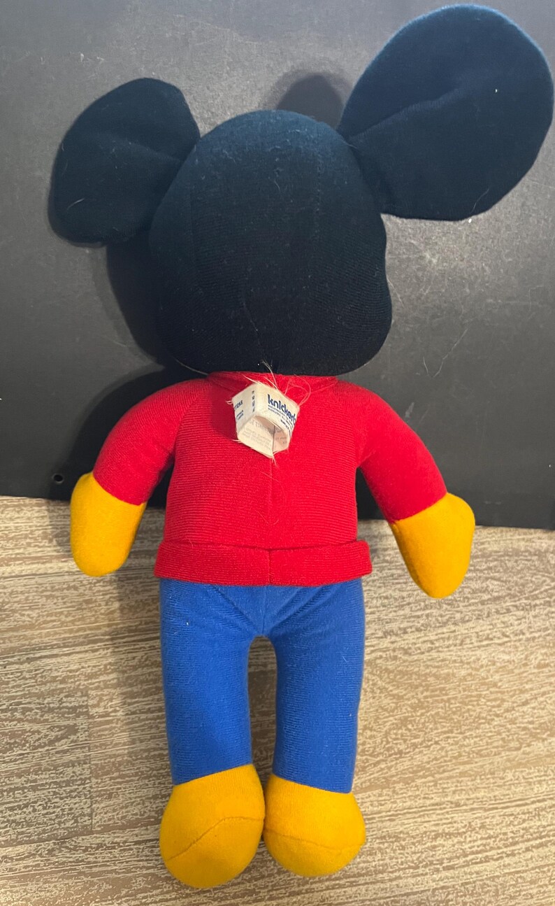May include: A red and blue plush Mickey Mouse toy with a black head and yellow shoes. The toy has a tag that says "Kiddie" on it.