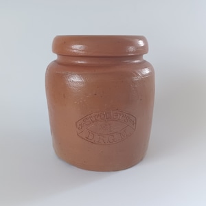 Puede incluir: Un tarro de cerámica marrón con tapa. El tarro tiene una etiqueta ovalada en relieve que dice "Stroder's #1 D.R.G.M."