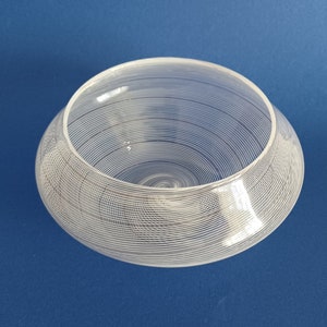 May include: A white glass bowl with a swirling, textured design. The bowl is round and has a wide, shallow opening.