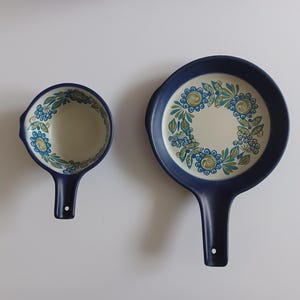 Könnte beinhalten: Zwei blaue Keramik-Kochgeschirrteile mit Blumendesigns. Ein kleiner Topf und eine größere Bratpfanne.