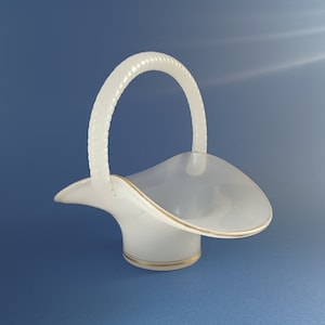 Puede incluir: Una cesta de cerámica blanca con un asa retorcida y un borde dorado. La cesta está diseñada para contener flores u otros objetos pequeños.