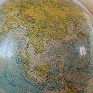 Könnte beinhalten: Ein Vintage-Globus in hellblauer und gelber Farbgebung. Der Globus zeigt die Kontinente Asien, Australien und Teile Afrikas. Der Globus ist aus Papier und hat einen Holzständer.