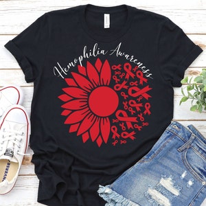 May include: Black t-shirt with a red sunflower design. The sunflower is made up of red ribbons that say "Hemophilia Awareness".