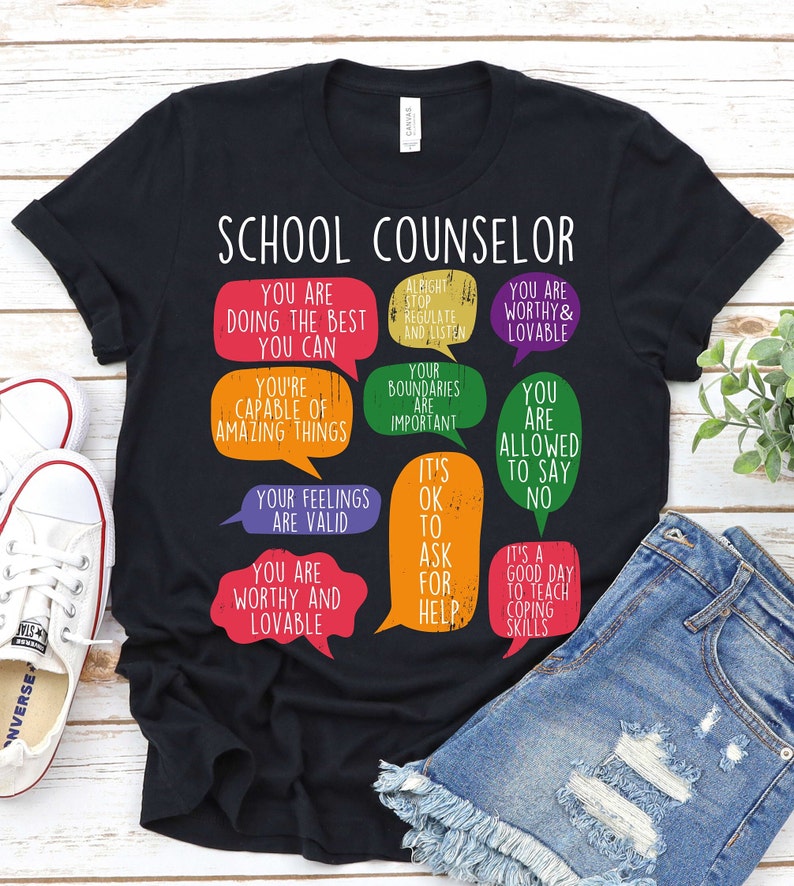 May include: Black t-shirt with a graphic of speech bubbles that say "School Counselor" and include phrases like "You are doing the best you can", "You are worthy and lovable", and "It's ok to ask for help".