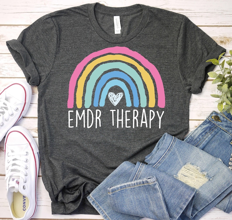K&ouml;nnte beinhalten: Ein dunkelgraues T-Shirt mit einem Regenbogen- und einem Herzmotiv. Der Text "EMDR THERAPY" ist unter dem Regenbogen aufgedruckt.