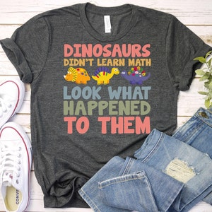 May include: A dark gray t-shirt with the text "Dinosaurs didn't learn math. Look what happened to them." in colorful letters. The text is surrounded by cartoon dinosaurs.
