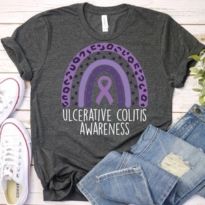 May include: A dark gray t-shirt with a purple ribbon and rainbow design. The text "Ulcerative Colitis Awareness" is printed below the design.