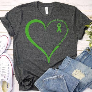 May include: A dark grey t-shirt with a green heart and a green ribbon. The text on the shirt reads "I wear green to fight  Pachys, Medulloblastoma and  Spinal Astrocytoma".