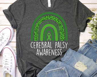 May include: A dark grey t-shirt with a green and white rainbow design. The rainbow has a green ribbon in the center and a leopard print pattern on the outer edges. The text "Cerebral Palsy Awareness" is printed in white below the rainbow.
