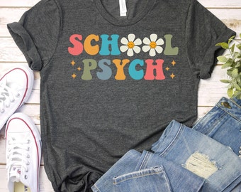 May include: A dark gray t-shirt with the text "SCHOOL PSYCH" in rainbow colors and white daisies with yellow smiley faces.