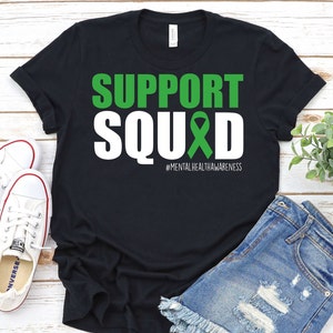 May include: Black t-shirt with white text that reads "SUPPORT SQUAD" with a green ribbon and the hashtag "#MENTALHEALTHAWARENESS".