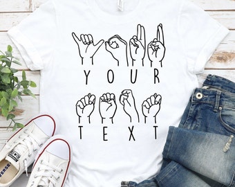 May include: White t-shirt with black line drawings of hands signing the letters "YOUR TEXT" in American Sign Language.
