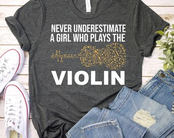 May include: A dark gray t-shirt with the text "Never underestimate a girl who plays the violin" and a violin silhouette made of musical notes.