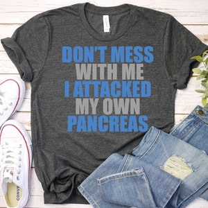 May include: A dark heather grey t-shirt with the text "Don't mess with me I attacked my own pancreas" in blue and grey lettering.