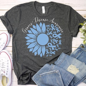May include: A dark gray t-shirt with a blue sunflower design. The sunflower is made up of blue ribbons and the text "Graves Disease Awareness" is written around the sunflower.
