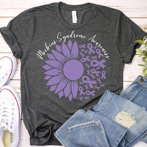 May include: A heather gray t-shirt with a purple sunflower design. The sunflower is made up of purple ribbons that say "Moebius Syndrome Awareness".