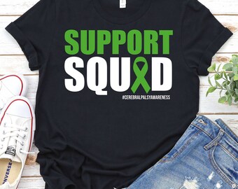 Może przedstawiać: Czarny T-shirt z białym napisem "SUPPORT SQUAD" z zieloną wstążką w środku słowa "SQUAD". Tekst pod wstążką brzmi "#CEREBRALPALSYAWARENESS".