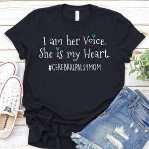 May include: Black t-shirt with white text that reads "I am her Voice. She is my Heart. #CerebralPalsyMom". The text is surrounded by two green hearts.