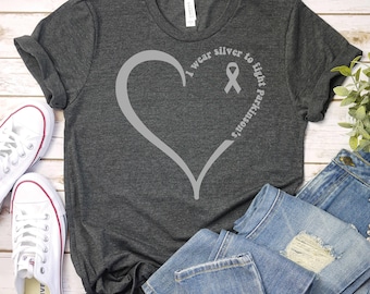 May include: A dark gray t-shirt with a silver heart and ribbon design. The text on the shirt reads "I wear silver to fight Parkinson's".