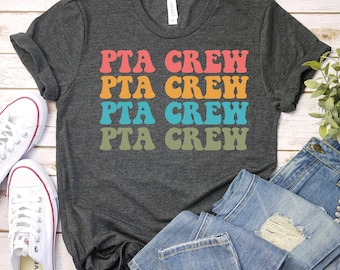 May include: A dark gray t-shirt with the text "PTA CREW" repeated four times in a retro font. Each word is a different color: red, orange, blue, and green.