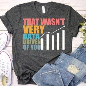 May include: A dark gray t-shirt with the text "That wasn't very data driven of you" in colorful letters with a white bar graph next to it.