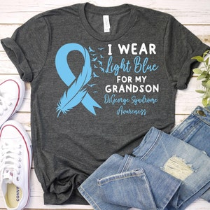 May include: A gray t-shirt with a light blue ribbon and the text "I wear light blue for my grandson DiGeorge Syndrome Awareness".