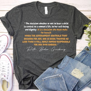 K&ouml;nnte beinhalten: Ein dunkelgraues T-Shirt mit einem Zitat von Ruth Bader Ginsburg &uuml;ber das Recht einer Frau, selbst zu entscheiden. Das Zitat lautet: "Die Entscheidung, ob man ein Kind zur Welt bringt oder nicht, ist von zentraler Bedeutung f&uuml;r das Leben einer Frau, f&uuml;r ihr Wohlbefinden und ihre W&uuml;rde. Es ist eine Entscheidung, die sie selbst treffen muss. Wenn die Regierung diese Entscheidung f&uuml;r sie trifft, wird sie als weniger als ein vollwertiger Erwachsener behandelt, der f&uuml;r seine eigenen Entscheidungen verantwortlich ist."