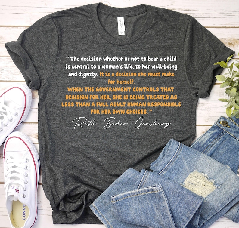 K&ouml;nnte beinhalten: Ein dunkelgraues T-Shirt mit einem Zitat von Ruth Bader Ginsburg &uuml;ber das Recht einer Frau, selbst zu entscheiden. Das Zitat lautet: "Die Entscheidung, ob man ein Kind zur Welt bringt oder nicht, ist von zentraler Bedeutung f&uuml;r das Leben einer Frau, f&uuml;r ihr Wohlbefinden und ihre W&uuml;rde. Es ist eine Entscheidung, die sie selbst treffen muss. Wenn die Regierung diese Entscheidung f&uuml;r sie trifft, wird sie als weniger als ein vollwertiger Erwachsener behandelt, der f&uuml;r seine eigenen Entscheidungen verantwortlich ist."