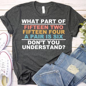 May include: A dark gray t-shirt with the text "WHAT PART OF FIFTEEN TWO FIFTEEN FOUR A PAIR IS SIX DON'T YOU UNDERSTAND?" printed in colorful letters.