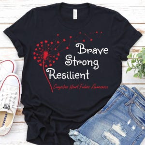 May include: Black t-shirt with the words "Brave Strong Resilient" in white, and a red dandelion design. The text "Congestive Heart Failure Awareness" is below the main text. The shirt is paired with denim shorts and white sneakers.