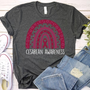 May include: A dark gray t-shirt with a pink and white rainbow design and the text "Cesarean Awareness".