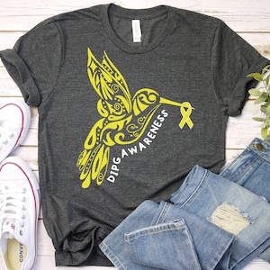 May include: A gray t-shirt with a yellow hummingbird design and the text "DIPG AWARENESS". A yellow ribbon is attached to the hummingbird's beak.